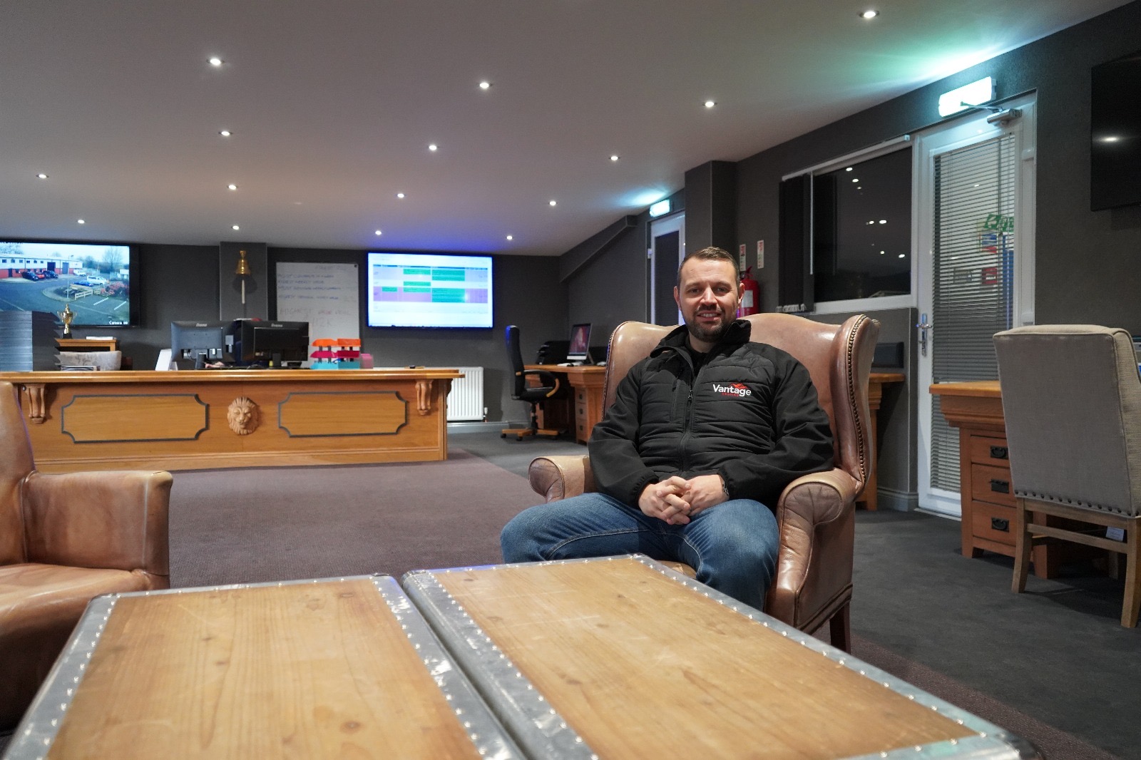 Male with dark hair and black fleece jacket sitting on a dark coloured armchair in the offices of Vantage Roofing